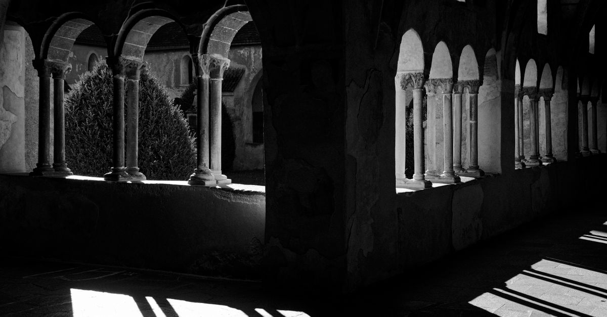 Black and white photo capturing sunlight casting shadows through cloister arches.