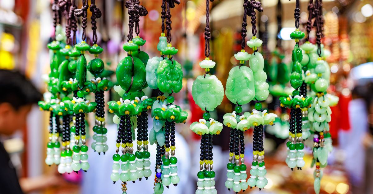 Vibrant green jade ornaments hang in a busy market, showcasing detailed craftsmanship and bright colors.