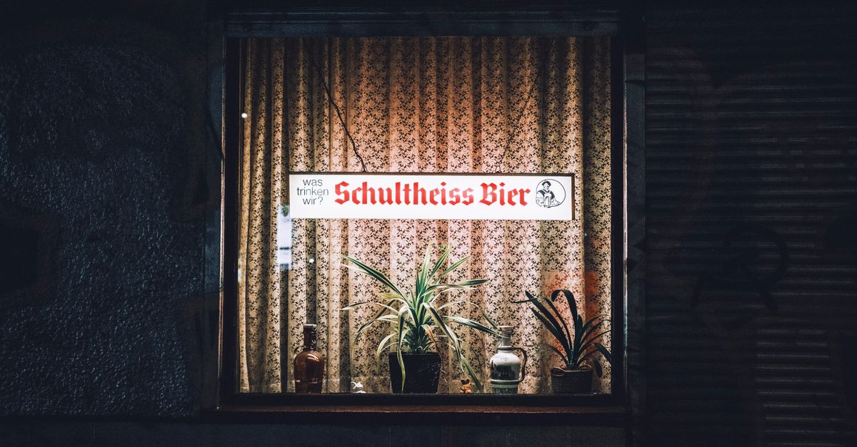 Cozy Berlin pub window display with illuminated sign and plants at night.