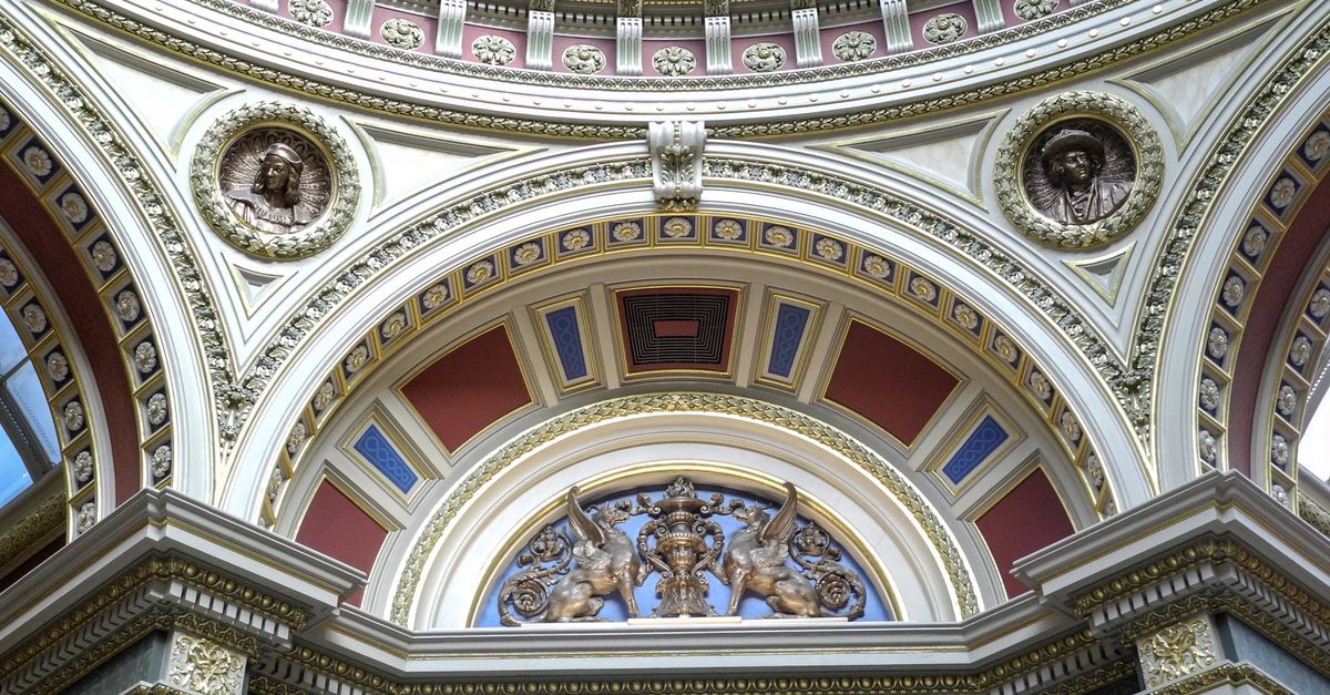 A grand architectural dome with intricate gold detailing and classical sculptures in a historic building.