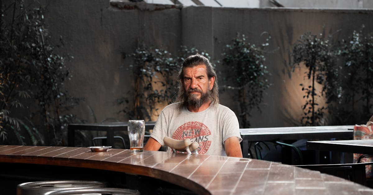 Man sitting at an outdoor bar with an empty glass, serene ambiance.
