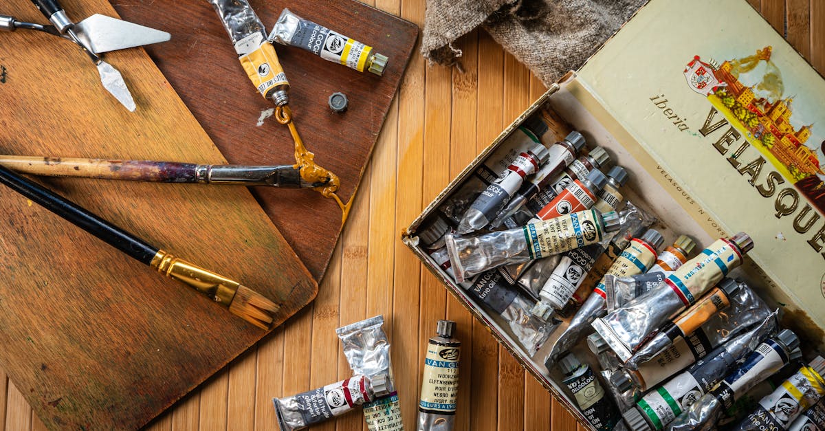 Artistic setup featuring various paint tubes, brushes, and tools on a wooden surface.