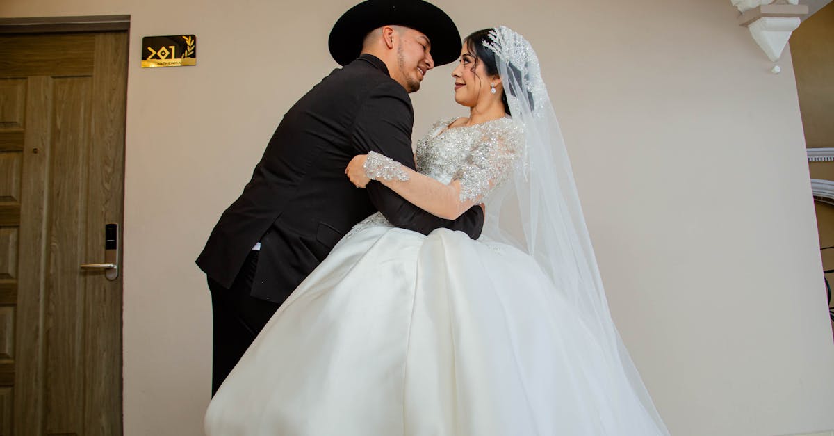 A bride and groom lovingly embrace in an elegant indoor setting, showcasing their wedding attire.