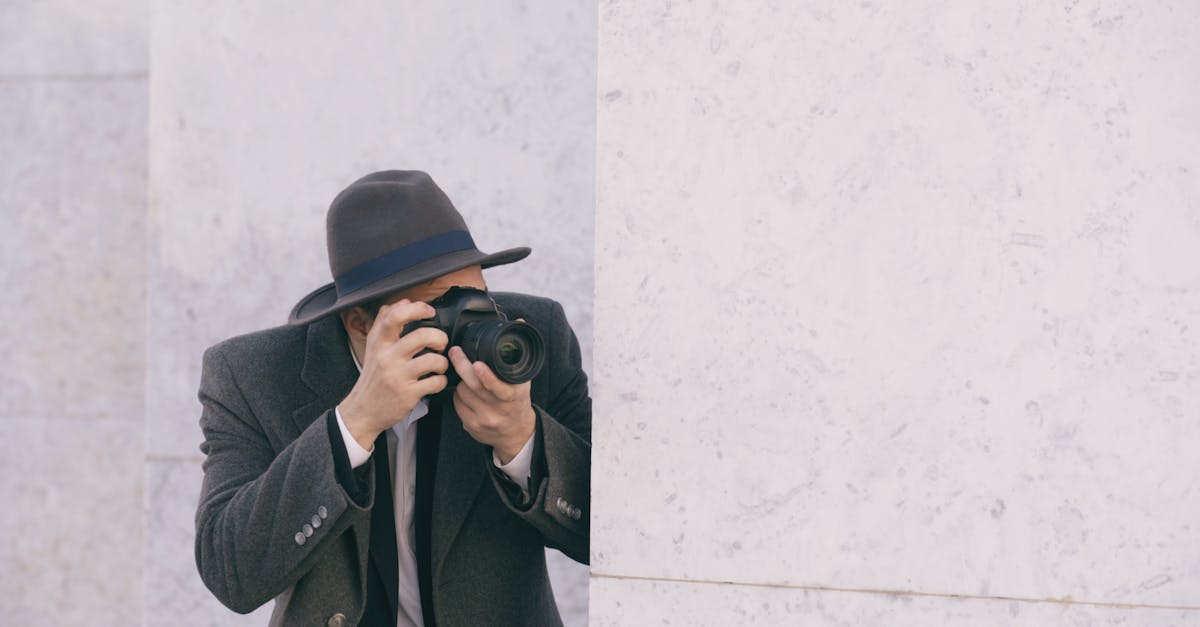 A person with a camera and gray hat capturing photos against a marble wall.