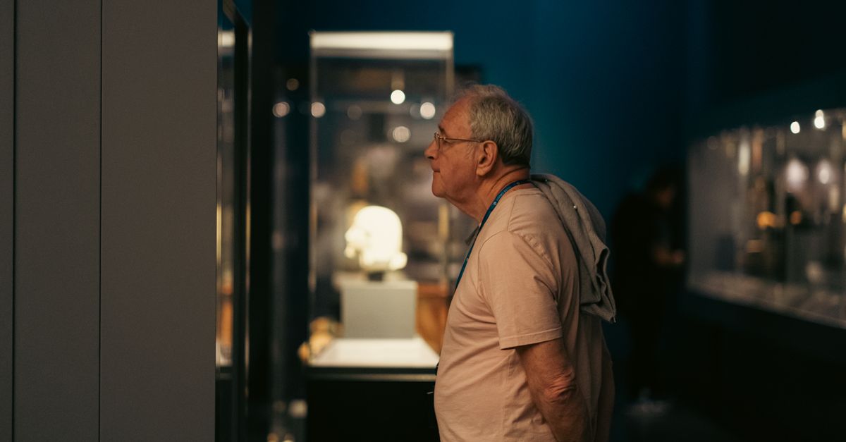 A senior man attentively explores exhibits in a dimly lit Budapest museum.