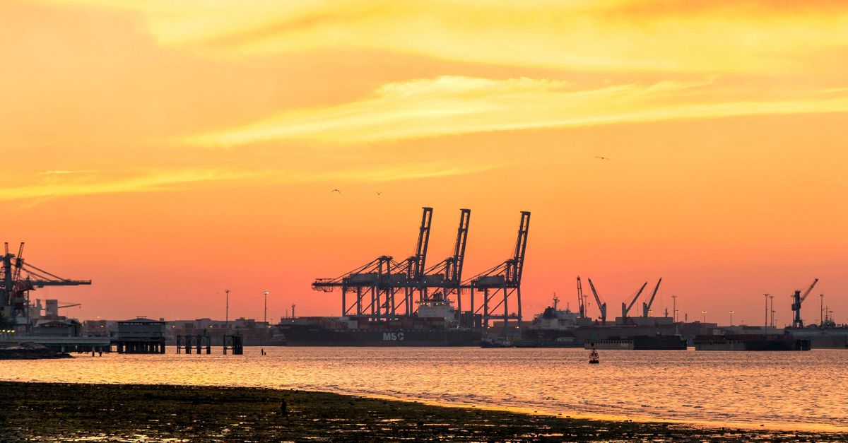 Vivid sunset over an industrial port with cranes silhouetted against the sky.