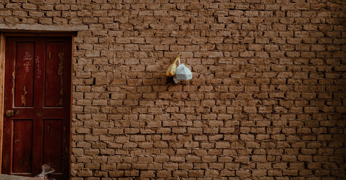 Muddy brick wall with red wooden door featuring inscriptions in Pacasmayo, Peru.