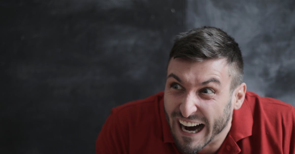 Portrait of a joyful man in a red polo shirt with a dynamic expression against a dark background.