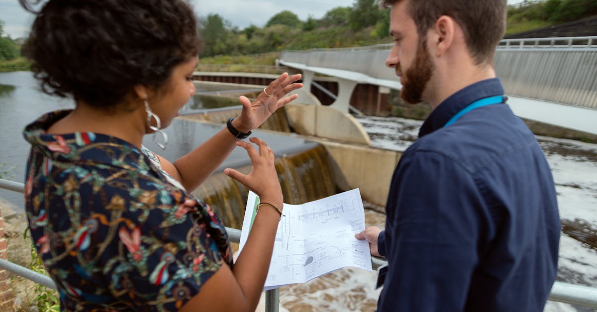 Two engineers discussing plans by a water project site. Collaborative teamwork on hydropower.