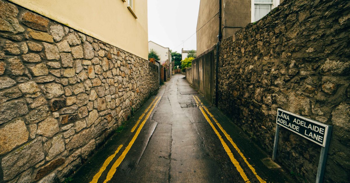 A narrow deserted alleyway in Dublin, with wet stone walls and a street sign.
