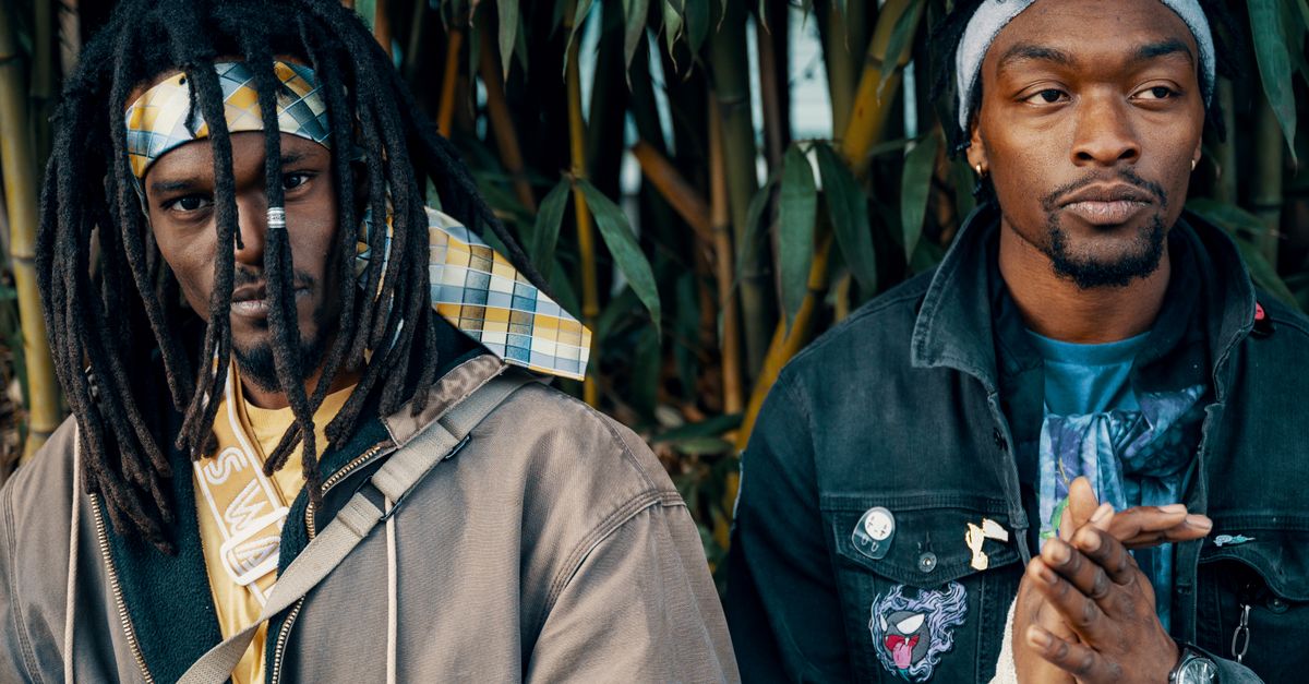 Two fashionable black men with dreadlocks and denim jackets posing outdoors, expressing urban style.