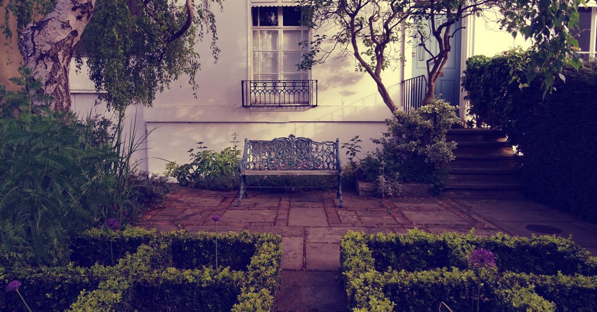A serene outdoor garden with a vintage bench framed by lush greenery and classic architecture.