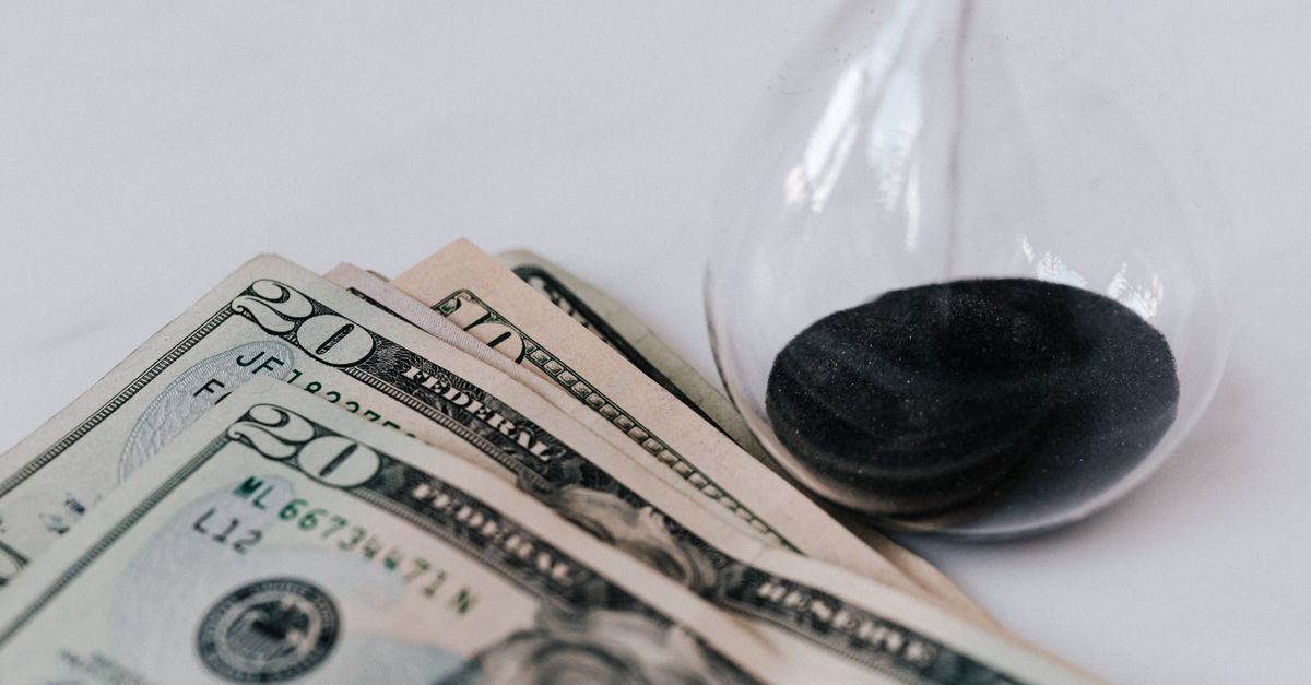 From above transparent hourglass with flares on fragile surface near pile of banknotes with numbers and official seal