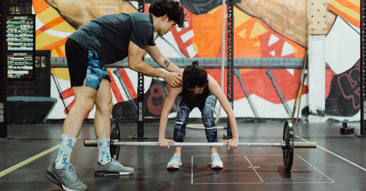 A coach instructs a young woman in proper barbell lifting technique at the gym.