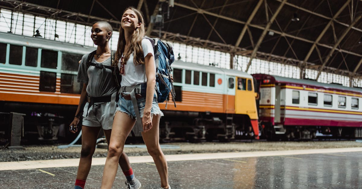Two women with backpacks walking and smiling at a railway station.