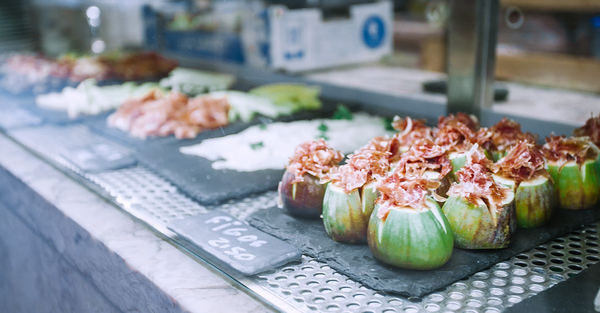 Appetizing fresh exotic stuffed figs served on counter with assorted foods in local market in sunlight