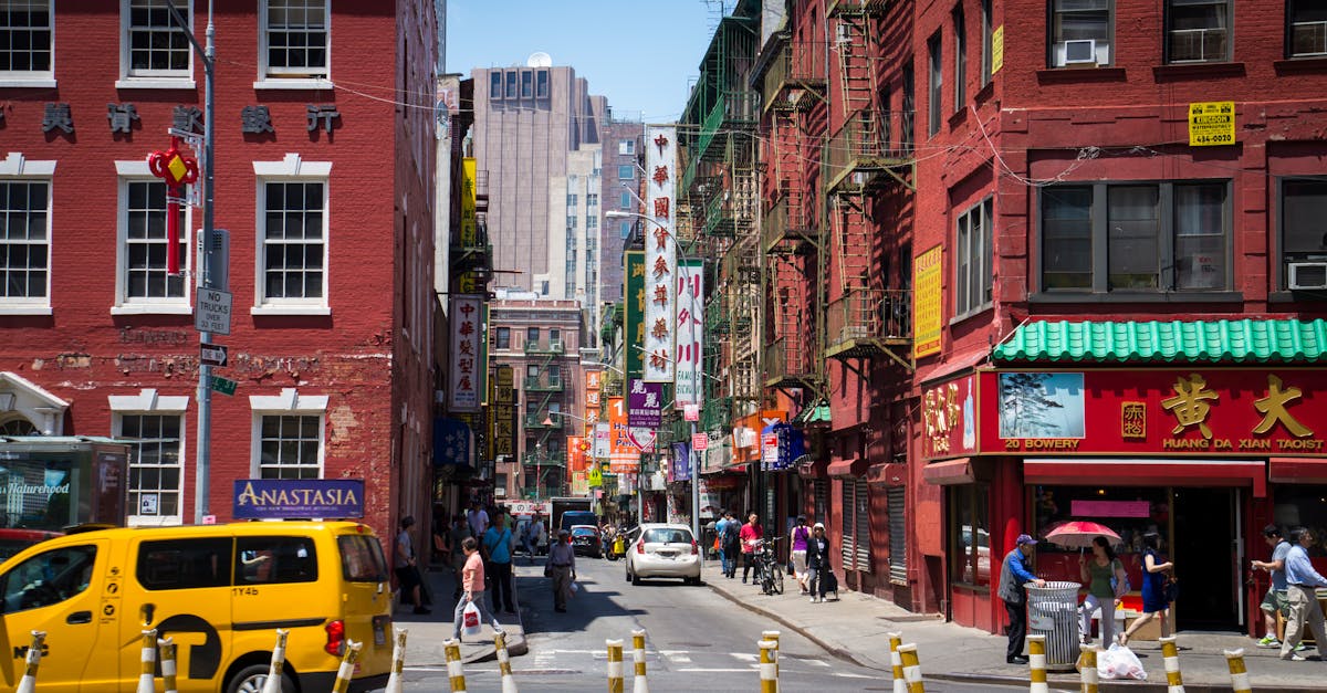 Busy daytime street scene in Chinatown, New York City with pedestrians, shops, and taxis.