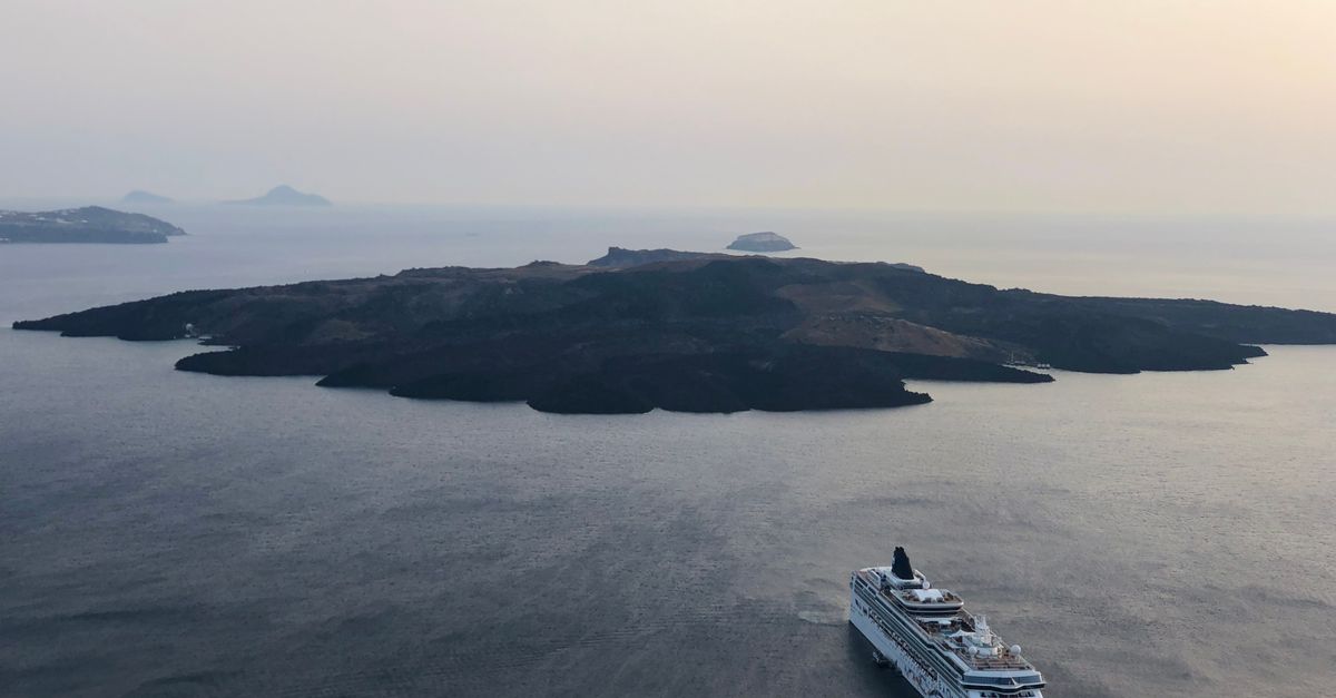 Stunning aerial shot of a cruise ship sailing near the volcanic island of Thira, Greece, at sunset.