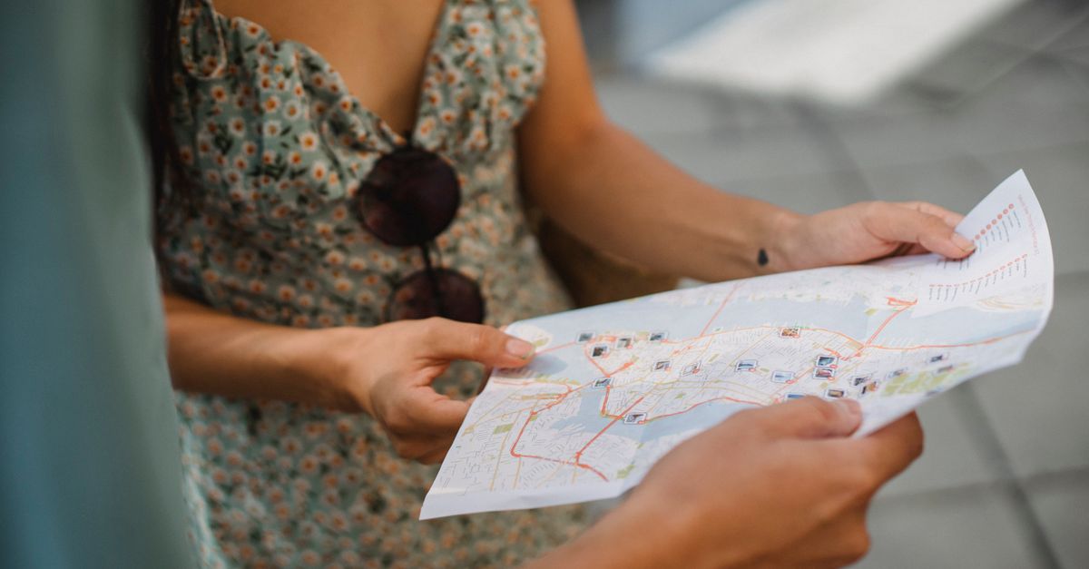 Crop anonymous couple travelers in summer clothes checking location in paper map while walking in unknown city