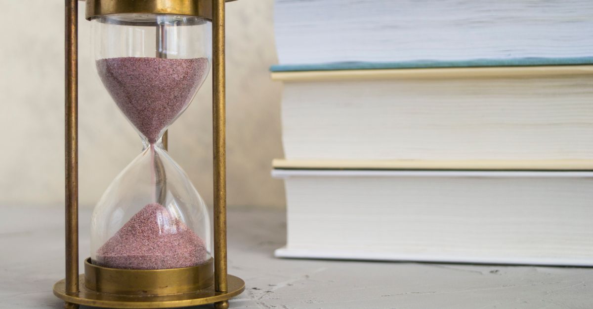 Close-up of hourglass with red sand beside stacked books, symbolizing time and knowledge.