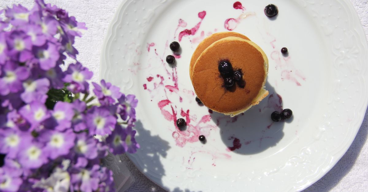 Top view of pancakes with blueberries on a white plate with garden verbena flowers.