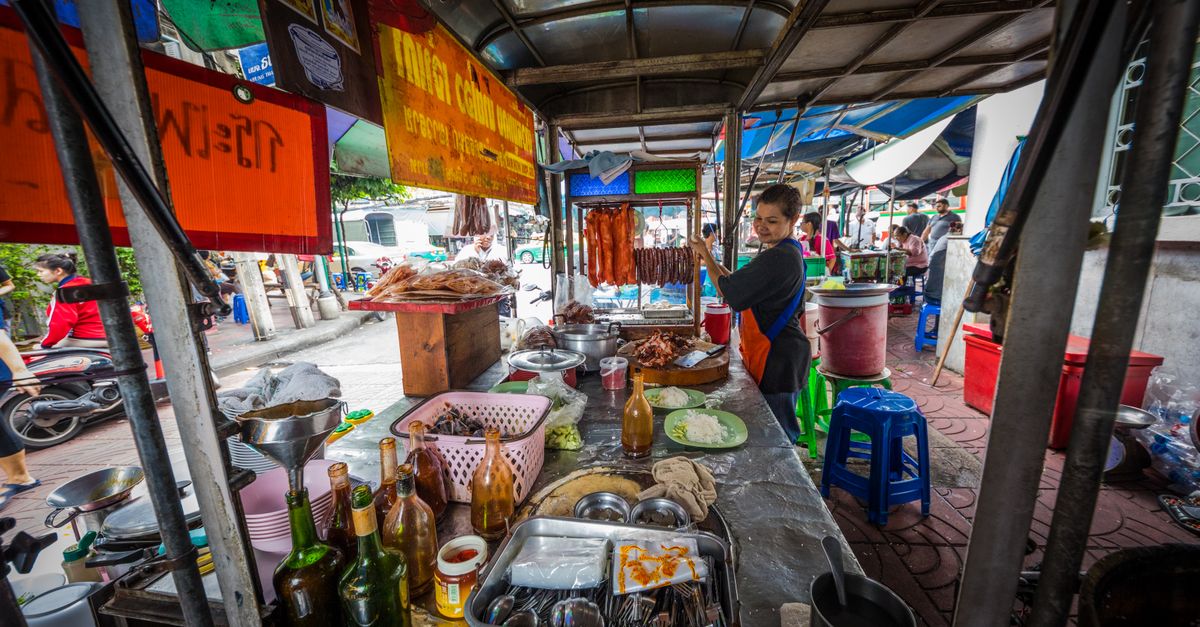 A vibrant street vendor prepares traditional Asian street food at a bustling outdoor market.