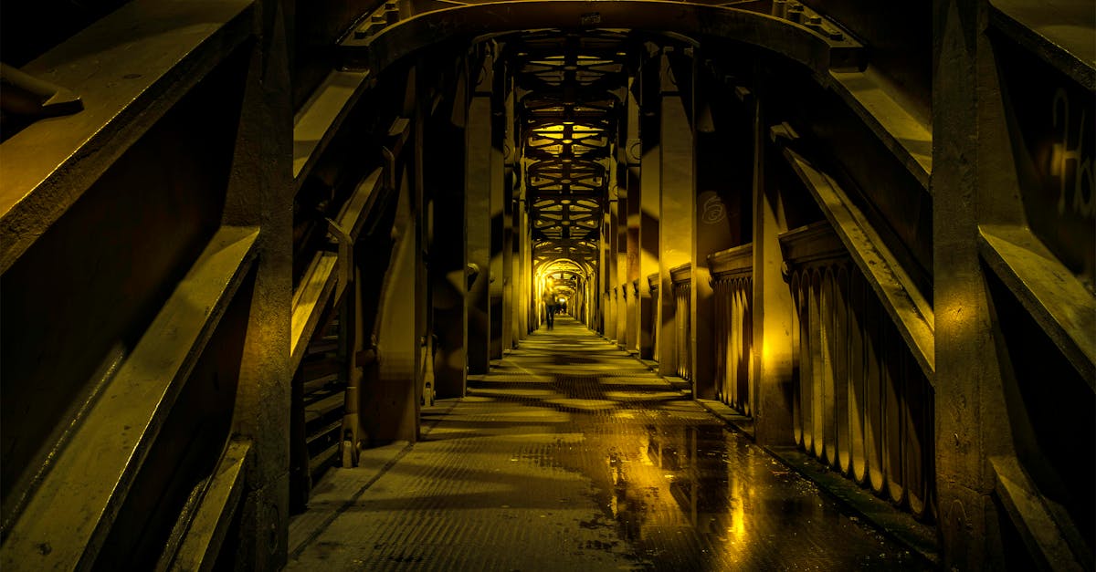 Eerie view inside a steel tunnel with reflections on puddles under dim lighting.