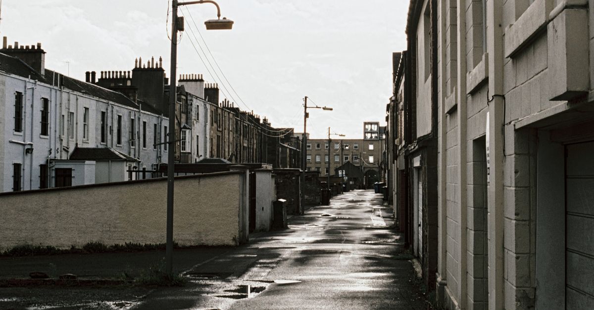 A nostalgic view of a wet, empty city street lined with classic buildings under overcast skies.