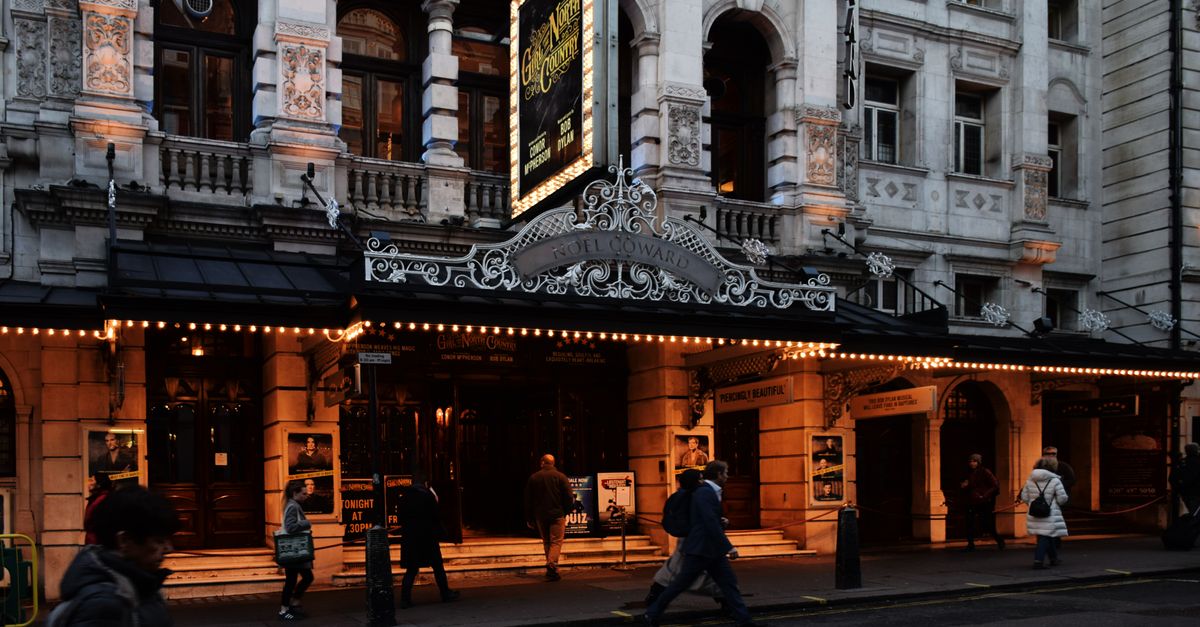 People walking by an illuminated theater in Central London at night, showcasing urban night life.