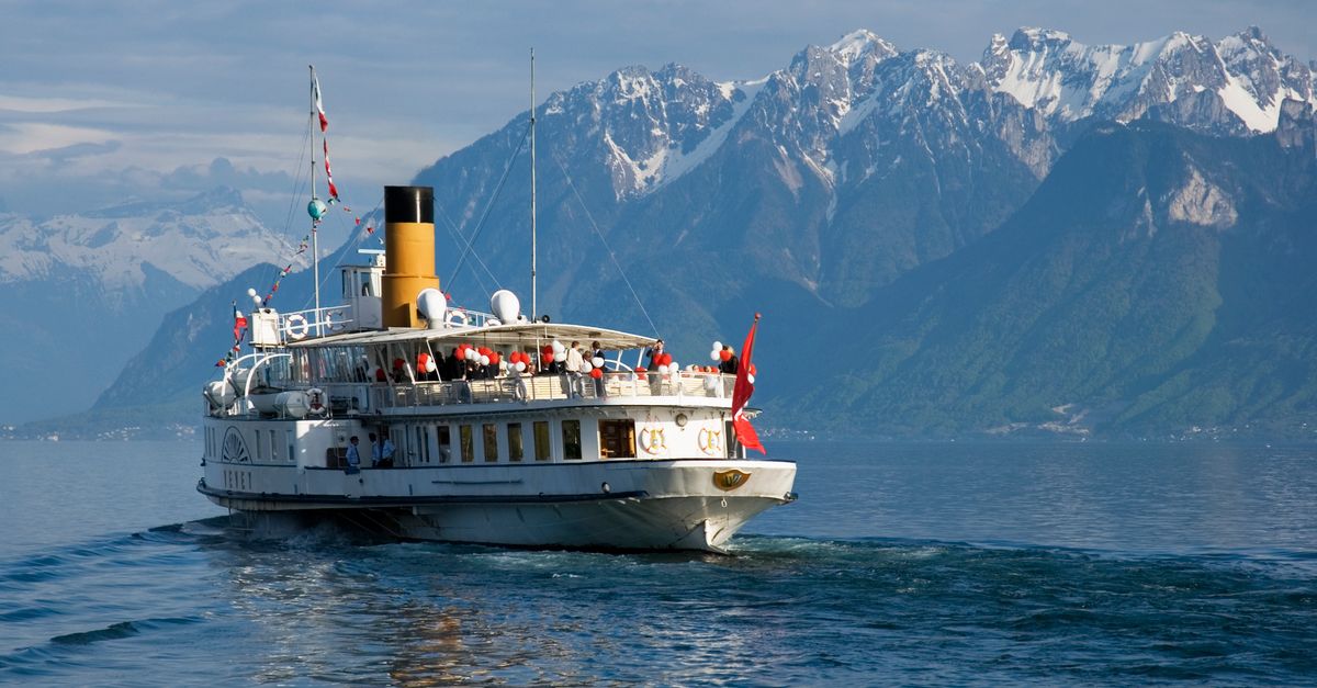 A scenic view of a historic paddle steamer cruising Lake Geneva with the Swiss Alps in the background.