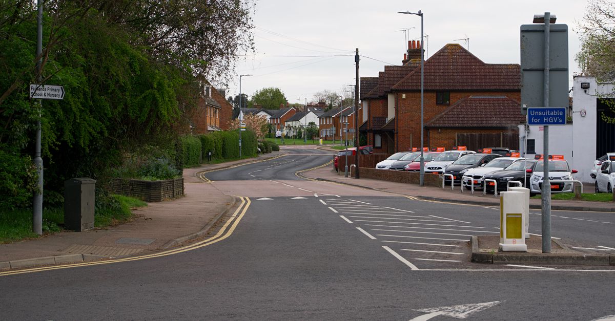 Serene suburban street in England, showcasing residential houses and road signs on a calm day.