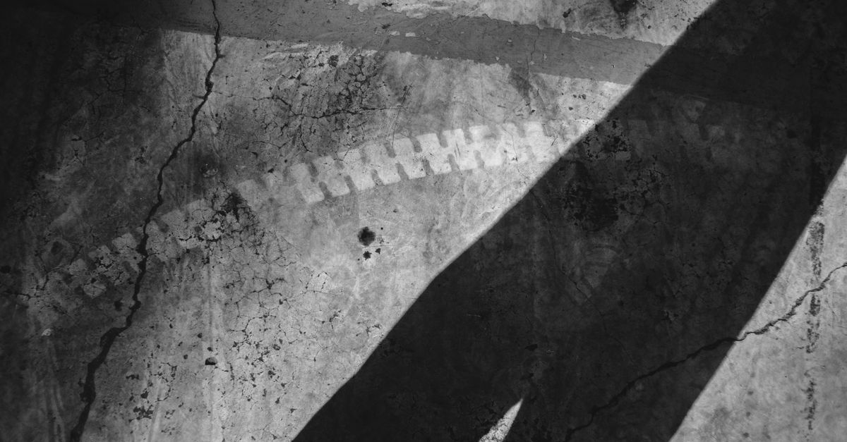 Black and white of linear shadow on cracked concrete wall with traces of dye