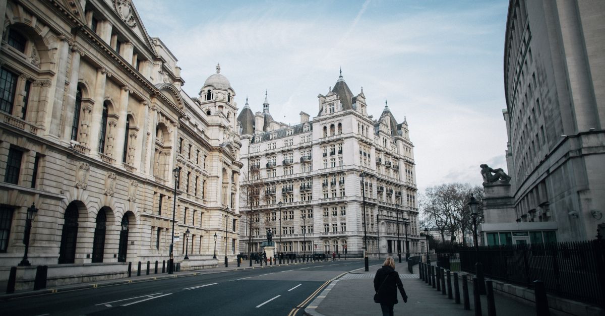 Back view of anonymous female strolling on walkway between road and aged masonry building exteriors in Whitehall London