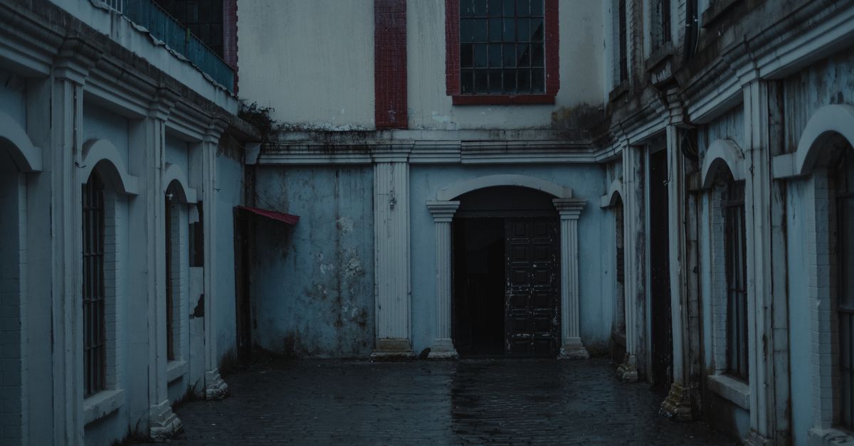 Paved sidewalk between aged neglected residential houses with windows located against arched passage on street in desolated district of city