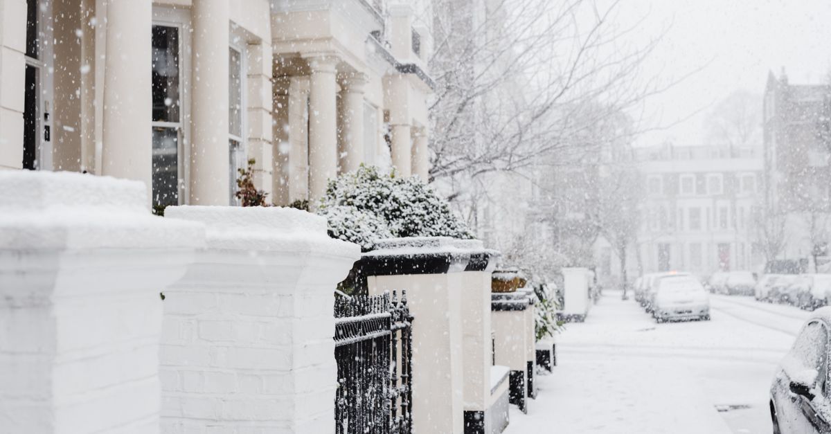 Snowy sidewalk between roadside with cars and residential houses with fences located in town on cold winter day during snowfall