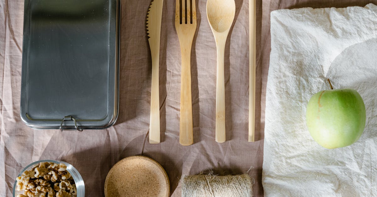 Sustainable flat lay arrangement with wooden utensils, green apple, and lunch box.