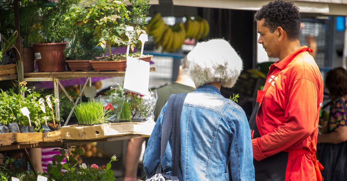 Man and woman engaging in lively street market conversation surrounded by fresh plants.