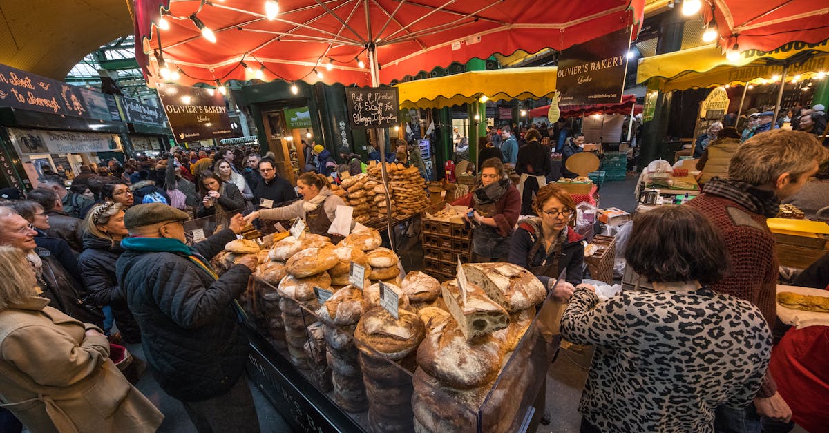 Bustling market scene at London's Borough Market with crowds buying artisan bread under colorful umbrellas.