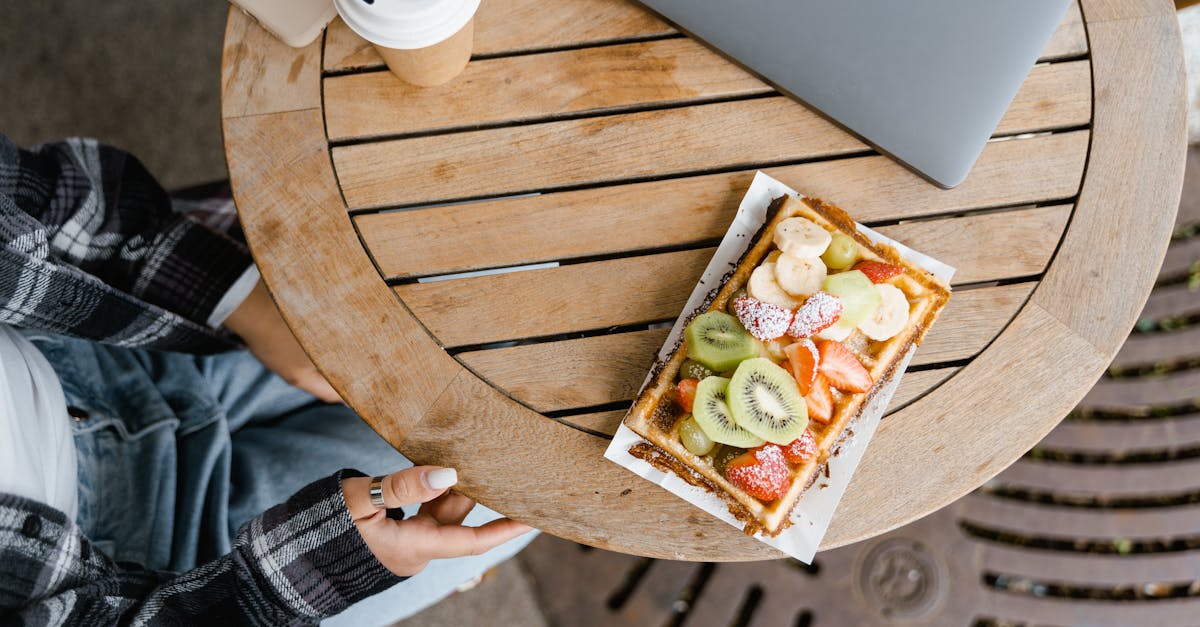 Delicious fruit-topped waffle on a wooden table with a coffee and laptop nearby.