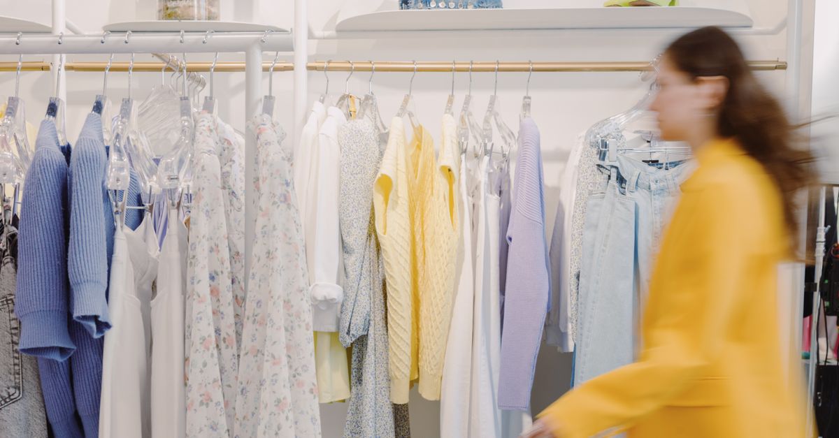Blurred woman walks by colorful clothes rack in indoor fashion store.