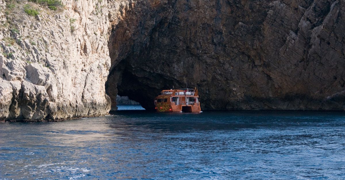 Explore the scenic beauty of a boat navigating through a stunning rock cave on a tranquil sea.