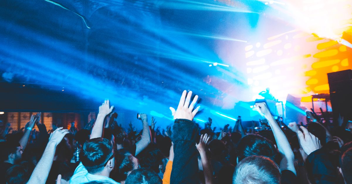 Excited nightclub crowd raising hands in vibrant lights, enjoying a live DJ set. Perfect for nightlife and music culture visuals.