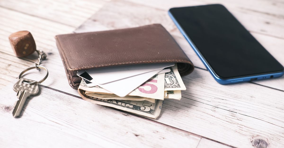 Close-up of a wallet with cash, smartphone, and keys on a wooden surface.