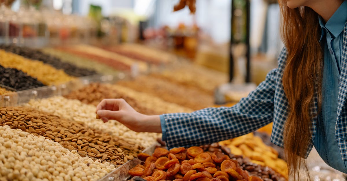 A woman is choosing a variety of nuts at an outdoor market stall, showcasing vibrant colors and textures.